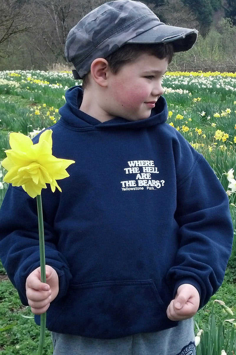 Child holding a yellow flower in a field with text on their hoodie.